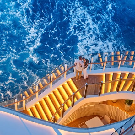 Par nyder udsigten på oplyste udendørs dækstrapper ombord på et Silversea-krydstogtskib med det dybblå hav nedenfor