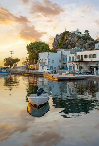 Hyggelig havnefront i Patmos by ved solnedgang med tavernaer, hvide huse og lille båd i vandet